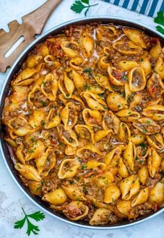 a pan filled with pasta and meat sauce on top of a table next to utensils