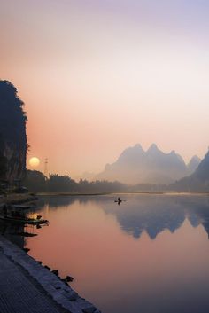 a body of water with mountains in the background at sunset or sunrise, near a dock