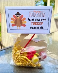 a turkey craft kit sitting on top of a table next to a sign that says happy thanksgiving paint your own turkey magnet kit