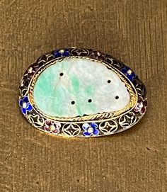 "At the center of this ornate brooch is an ornate carved jade piece set in a vermeil setting surrounded by small pink/purple and blue enamel flowers. It is about 1 1/2\" long and 1\" long. It is marked 925 and is in wonderful preloved condition. Please see all photos for details and condition. Thank you for looking!" Ornate Oval Carved Brooches, Ornate Carved Oval Brooches, Ornate Carved Collectible Brooches, Traditional Gemstone Brooches For Gift, Traditional Gemstone Brooches As Gift, Heirloom Style Carved Brooch For Gifts, Heirloom Carved Brooches As Gift, Ornate Gemstone Brooches For Collectors, Traditional Collectible Round Brooches