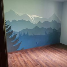 an empty room with mountains painted on the wall and wood flooring in front of it