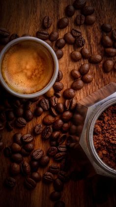 coffee beans and ground coffee on a wooden table next to a cup with liquid in it