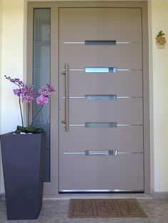 a tall vase with flowers in it next to a front door that has glass panels on the side