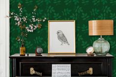 a green wall with a bird on it next to a lamp and vase filled with flowers