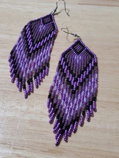 two pairs of purple beaded earrings sitting on top of a wooden table