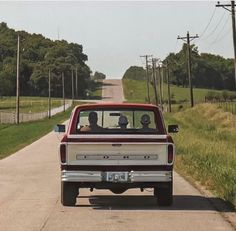 a red and white truck driving down a road next to a lush green field with trees