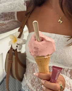 a woman holding an ice cream cone with pink frosting on it and a tube of lip balm in her hand