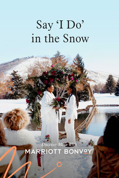 two women in white dresses standing next to each other on snow covered ground with trees and mountains behind them