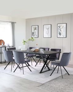 a dining room table with purple chairs and pictures on the wall behind it in front of a window