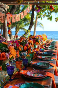 a long table is set up with colorful plates and place settings for an outdoor dinner