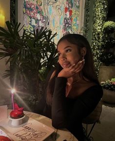 a woman sitting at a table in front of a cake with a candle on it