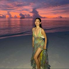 a woman standing on top of a sandy beach next to the ocean at sunset with clouds in the sky