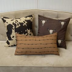 three pillows are sitting on a couch with barbed wire in the back and cow heads on them