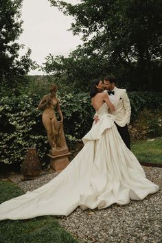 a bride and groom kissing in front of a statue