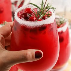 a hand holding a wine glass filled with red liquid and topped with sprigs