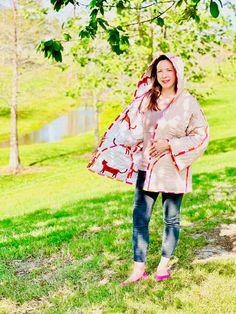 a woman standing under a tree wearing a pink raincoat and holding a red umbrella