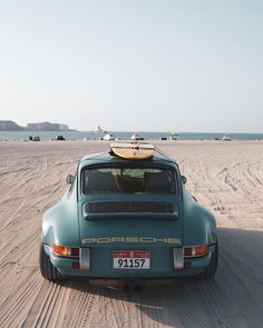 a blue car with a surfboard on the roof sits in the sand at the beach