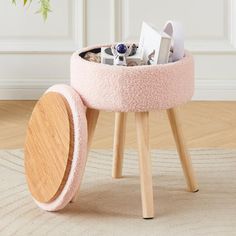 a small pink stool with a wooden base and wheels on the floor next to a potted plant