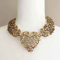 "Avon Jose and Maria Barrera necklace. Gold tone with rhinestones. This one has definite Victorian vibes with it's intricate scrolling. Adjustable length--at longest is around 14.5\". Can be adjusted to be more of a choker. Heavy. Signed Barrera on back. Does have some discoloration, but all stones are present. Please look closely at photos. Bib measurement of 2\" is the measurement of the heart. Thanks for visiting the shop! Make sure to stop back by!" Vintage Gold Rhinestone Necklace With Sparkling Stones, Metal Rhinestone Necklace For Anniversary, Elegant Antique Gold Necklaces For Anniversary, Gold Crystal Necklace With Intricate Design, Gold Necklaces With Intricate Crystal Design, Gold Necklace With Intricate Crystal Design, Intricate Design Gold Necklace In Crystal, Antique Gold Jewelry With Rhinestones, Antique Gold Filigree Necklaces For Anniversary