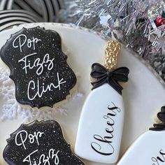 three decorated cookies with black and white icing on a platter next to silver tinsel