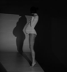 a woman is standing in the dark with her shadow on the wall behind her,