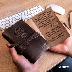 a person holding a brown leather book on top of a desk next to a keyboard