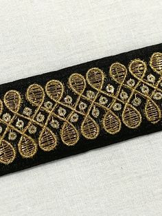 a black and gold ribbon with intricate designs on it's side, sitting on a white surface