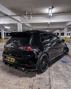 the back end of a black car parked in a parking garage with no one around