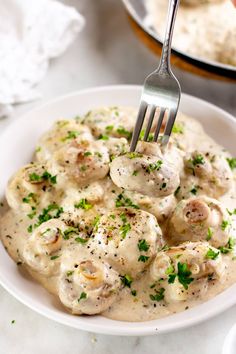 a white plate topped with dumplings covered in gravy next to a fork