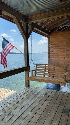 an american flag hanging from a porch swing on a dock overlooking the water with a boat in the distance