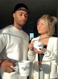 a man and woman standing next to each other with coffee cups in their hands,