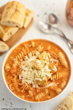 a bowl of pasta soup with bread on the side