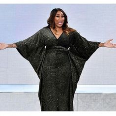 a woman standing in front of a screen with her hands out and wearing a black dress