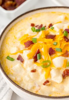 a bowl of potato soup with bacon, cheese and green onions on the side is ready to be eaten