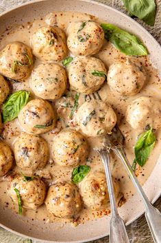 a white bowl filled with meatballs covered in gravy and garnished with basil