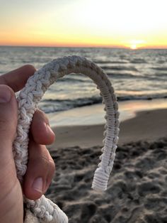 a hand holding a white rope on top of a beach next to the ocean at sunset