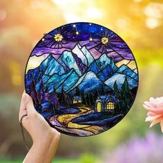 a hand holding up a stained glass plate with mountains in the background