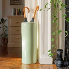 two umbrellas in a green container on the floor next to a potted plant