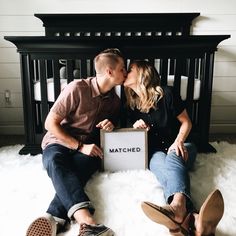 a man and woman kissing while sitting on the floor in front of a baby crib