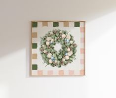 a christmas wreath is hanging on the wall above a framed canvas with ornaments and greenery