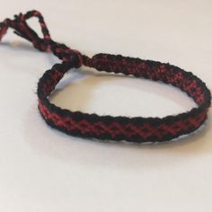 a red and black rope bracelet on a white surface with a knot at the end