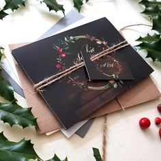 two christmas cards with holly and berries tied to each other on top of envelopes