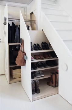 an open closet with shoes and handbags in the bottom shelf, under stairs leading up to second floor