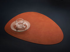 a glass cup and saucer sitting on top of a brown place mat with a black background