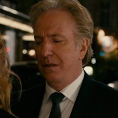 a man in a suit and tie standing next to a woman on the street at night