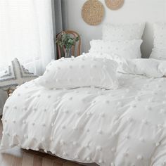 a bed with white comforters and pillows in a room next to a window,