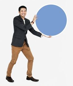 a man in a suit and brown pants holding a large blue object up to his face