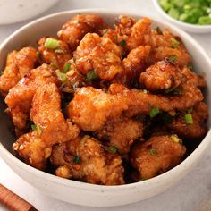 a white bowl filled with fried chicken and garnished with green onions