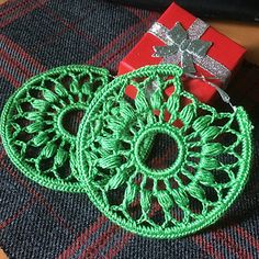 two green crocheted doily are next to a red box with a silver bow