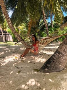 a woman sitting in a hammock between two palm trees on the beach,